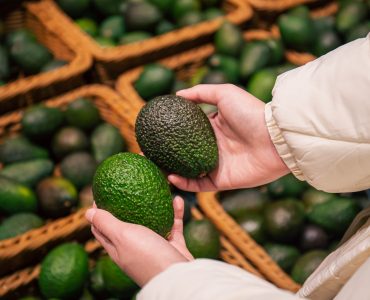A woman chooses an avocado in a grocery store. A woman chooses an avocado in a grocery store, close-up, buying organic food for cooking.