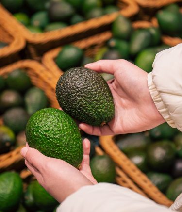A woman chooses an avocado in a grocery store, close-up, buying organic food for cooking.