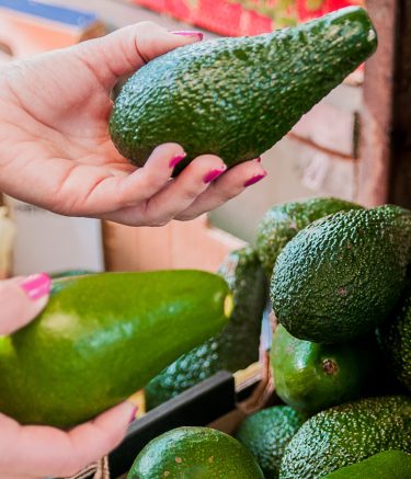 Cropped image of a customer choosing avocados in the supermarket. close up of woman hand holding avocado in market. sale, shopping, food, consumerism and people concept