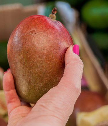 Happy young woman customer choosing ripe mango fruit on market. woman picking up, choosing fruits, mango. girl with mango fruit in grocery store. Mango good for skin, concept